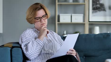 Penisve-Old-Senior-Woman-Reading-Agreement,-Sitting-on-Sofa