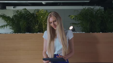 Relaxing-woman-with-tablet-in-office.-Young-elegant-woman-sitting-barefoot-on-wooden-tribune-in-modern-office-using-tablet-and-taking-rest