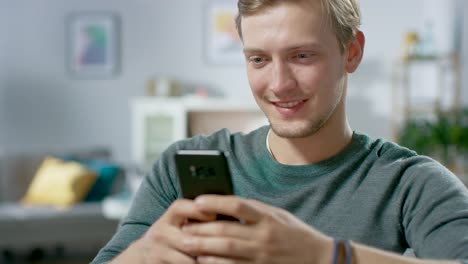 Retrato-del-guapo-joven-hombre-utilizando-Smartphone,-navegación-en-Internet,-revisar-redes-sociales-mientras-se-sienta-en-casa.