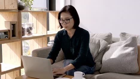 Schöne-Asiaten-junge-Frau,-arbeiten-mit-Computer-Laptop-und-Kaffeetrinken-beim-Sitzen-auf-dem-Sofa-zu-Hause.-Arbeit-zu-Hause-Konzept