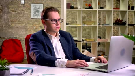 Upset-caucasian-man-stopped-his-work-at-the-table-on-laptop-thinking-and-looking-straight,-indoor,-office-vibes