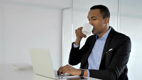 Lässige-afroamerikanischer-Geschäftsmann-trinken-Kaffee-während-der-Arbeit-am-Laptop