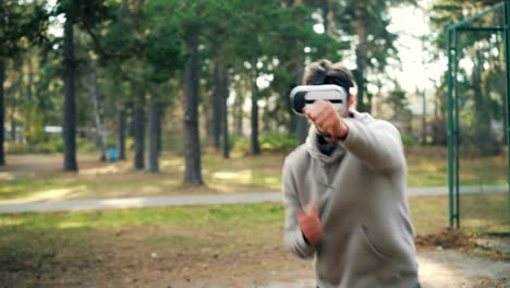 Active-guy-is-wearing-augmented-reality-glasses-and-boxing-enjoying-fighting-simulation-in-gadget-during-training-in-park.-Youth,-sports-and-fun-concept.