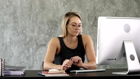 Young-professional-woman-sitting-down-at-the-desk-and-working-with-computer