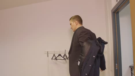 Junger-Geschäftsmann-Eingabe-im-Büro-Mantel-ausziehen-und-Kleiderbügel-hängen