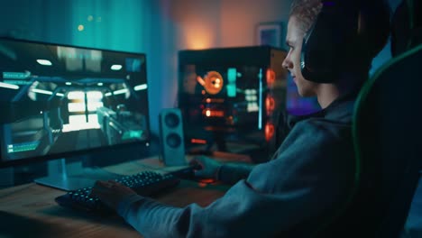 Spieler-setzt-seine-Kopfhörer-mit-Mikrofon-auf-und-startet-die-Wiedergabe-von-Online-Shooter-Videospiel-auf-seinem-persönlichen-Computer.-Zimmer-und-PC-haben-bunte-Neonlichter-geführt.-Gemütlichen-Sie-Abend-zu-Hause.