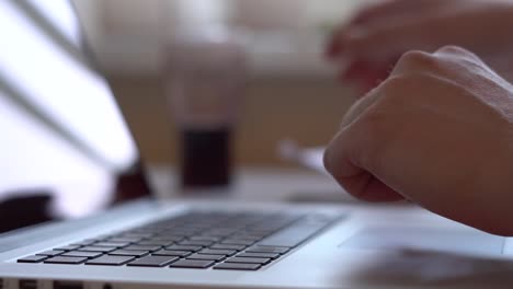 Closeup-of-hands-working-and-typing-on-a-laptop-keyboard-with-black-keys,-in-the-process-of-work-a-man-looks-at-paper-documents