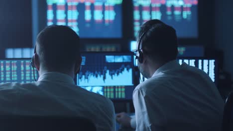 Team-of-stockbrokers-are-having-a-discussion-in-a-dark-office-with-display-screens.