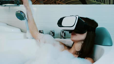 Girl-take-bath-full-of-foam-in-bathroom-with-virtual-reality-glasses.-Laugh