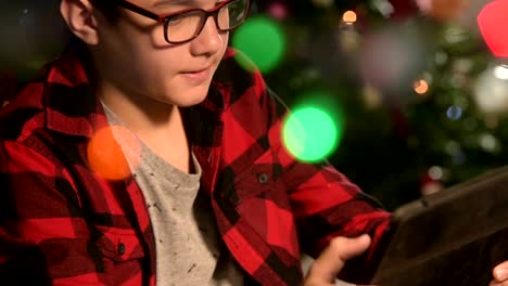 Young-Boy,-child-looks-to-the-tablet-lying-on-sofa.On-the-background-lights-garlands