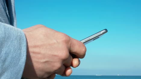 Man-Using-Mobile-By-The-Sea-In-A-Sunny-Day