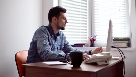 Junger-Geschäftsmann-auf-Computer-in-stilvollen-modernen-Büro-arbeiten.-Computer,-Telefon-und-Tasse-auf-den-Tisch.-Schuss-in-4k