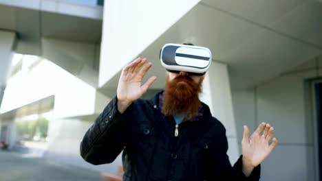 Dolly-shot-of-Young-bearded-man-using-virtual-reality-headset-for-360-VR-experience-and-take-of-glasses-smiling-outdoors