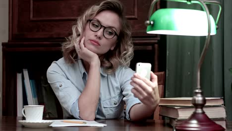 Young-woman-in-glasses-making-selfies-on-the-phone-at-her-workplace