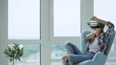 Junge-Frau-haben-VR-Erlebnis-mit-virtual-Reality-Kopfhörer-sitzen-im-Stuhl-auf-Balkon