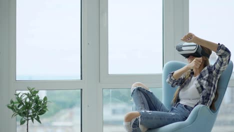 Young-woman-have-VR-experience-using-virtual-reality-headset-sitting-in-chair-on-balcony