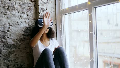 Curly-african-american-woman-getting-experience-using-VR-360-headset-glasses-of-virtual-reality-at-home