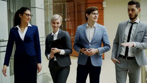 Stedicam-tiro-grupo-de-jóvenes-empresarios-hablando-y-caminando-en-el-vestíbulo-de-la-oficina