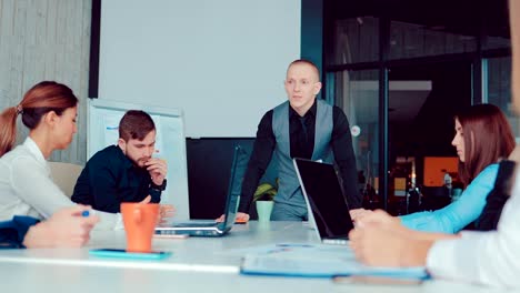 Boss-is-standing-with-his-hands-on-the-table-and-talking-with-business-people-in-a-modern-office