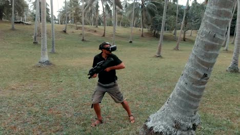 Man-with-weapon-playing-virtual-reality-game-in-the-jungle,-drone-shot