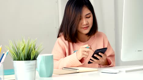 Junge-asiatische-Frauen-Unternehmer-mit-Smartphone-und-nehmen-Notizen-app-im-Büro.