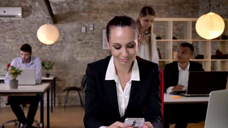 Young-businesswoman-is-reading-and-typing-message-on-smartphone-in-office,-her-colleagues-are-networking-with-technologies,-working-concept,-business-concept,-communication-concept