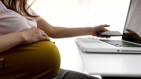 Mujer-embarazada-trabajando-con-el-ordenador-portátil-y-teléfono