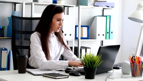 Frau-auf-Kopfhörer-sprechen-und-mit-Laptop-im-modernen-Büro