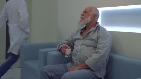 Senior-man-sit-on-sofa-in-clinic-and-wait-his-turn