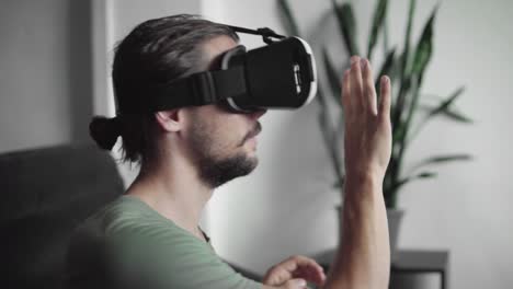 Junge-bärtige-Hipster-Mann-mit-seinem-VR-Kopfhörer-Anzeige-für-virtual-Reality-Spiel-oder-das-360-Viedeo-und-versuchen,-etwas-zu-berühren,-er-sehen-und-fangen-beim-Sitzen-auf-dem-Sofa.-VR-Technologie.