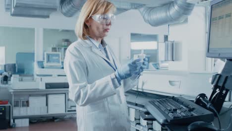 In-Laboratory-Female-Scientist-Takes-Out-Test-Tube-with-Blood-Samples-Out-of-the-Medical-Equipment-and-Analyzes-Data-with-Personal-Computer.-Team-of-Researchers-Work-in-Pharmaceutical-Laboratory.