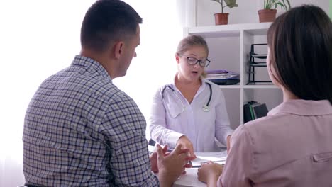 female-doctor-telling-bad-news-about-health-to-young-couple,-man-comforting-his-sad-wife-in-medical-office