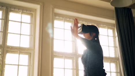 Niña-riendo-en-suéter-está-teniendo-diversión-con-gafas-de-realidad-virtual-moviendo-las-manos-en-light-studio-con-gafas-en-la-cabeza-y-disfrutando-de-gadget.