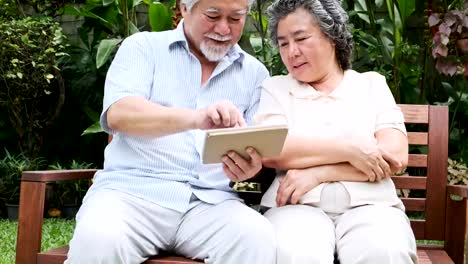 Senior-couple-sitting-and-using-tablet-together-in-home-garden.