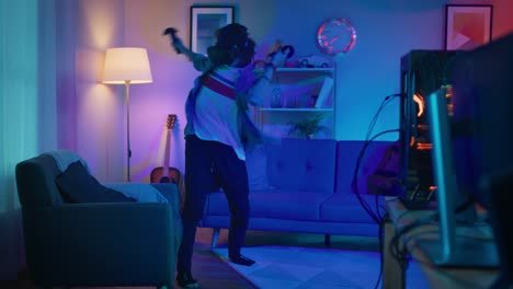 Young-Man-is-Energetically-Playing-a-Virtual-Reality-Video-Game-While-Wearing-a-Headset.-He's-is-Standing-in-a-Cozy-Room-with-Warm-Neon-Lights.-He's-Swinging-Hands,-Shooting-and-Dodging-Obstacles.