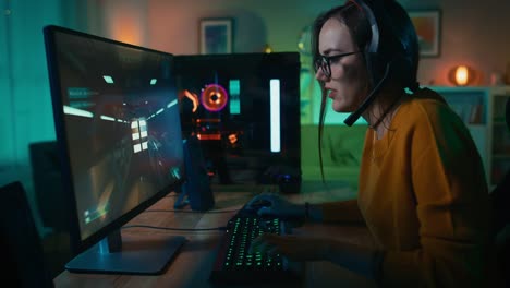 Excited-Gamer-Girl-in-Headset-with-a-Mic-Playing-Online-Video-Game-on-Her-Personal-Computer.-She-Talks-to-Other-Players.-Room-and-PC-have-Colorful-Warm-Neon-Led-Lights.-Cozy-Evening-at-Home.