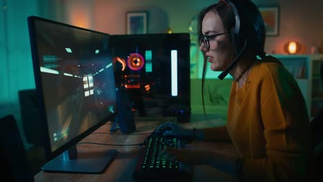 Begeistert-Gamer-Mädchen-im-Kopfhörer-mit-einem-Mikrofon-Online-Video-Spiel-auf-ihrem-PC-spielen.-Sie-spricht-mit-anderen-Spielern.-Zimmer-und-PC-haben-bunte-warme-Led-Neonlichter.-Gemütlichen-Sie-Abend-zu-Hause.