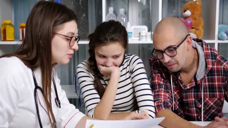 Father-with-his-teenager-daughter-on-examination-in-the-seed-doctor's-office-in-the-clinic.-The-doctor-reassures-the-teenager-girl-patient.