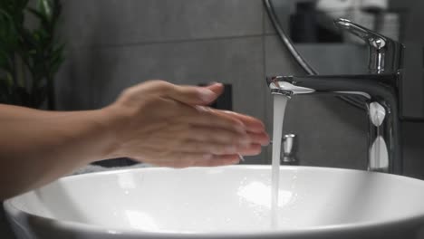 Woman-is-washing-and-lathering-hands,-rubbing-fingers-with-soap-in-sink.-Coronavirus-pandemic-prevention.-Female-washes-hands-in-sink-with-foam-to-wash-skin-and-water-flows-through-hands