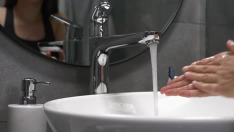 Caucasian-woman-is-washing-hands-with-soap-in-sink.-Female-in-modern-bathroom-washes-hands-with-foam,-rubbing-fingers,-water-flows-through-hands-to-prevent-coronavirus-pandemic