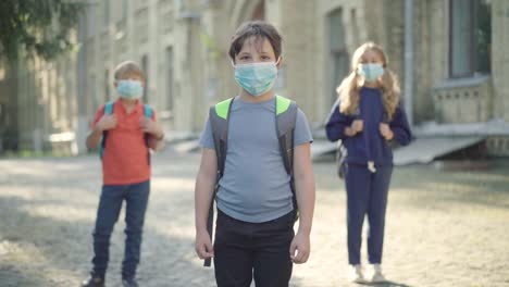 Middle-school-students-in-face-masks-having-fun-on-schoolyard-on-sunny-day.-Portrait-of-relaxed-positive-Caucasian-pupils-running-away.-Children-enjoying-leisure-after-studying-on-Covid-19-pandemic.