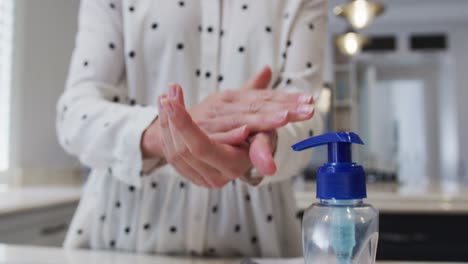 Mid-section-of-woman-sanitizing-her-hands-at-home