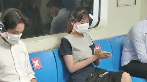 New-normal-lifestyle,-group-of-asia-passenger-various-professions-on-metro-subway-train-wearing-mask,-woman-uses-hand-sanitizer-liquid,-keep-social-distancing.-Protection-Section-of-pandemic-covid-19