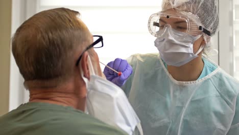 Krankenhausmitarbeiter-in-einem-Schutzanzug-nimmt-einen-Tupfer-von-einem-älteren-Patienten-für-Coronavirus