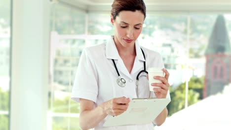 Beautiful-doctor-reading-files-and-looking-at-camera