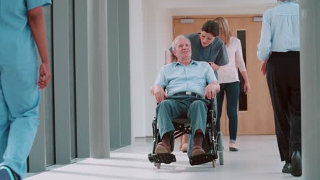 Nurse-Pushing-Senior-Patient-In-Wheelchair-Along-Corridor