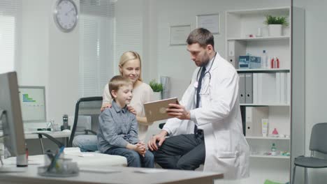 Male-Doctor-Consults-Young-Boy-and-His-Mother-with-a-Help-of-a-Tablet.-They-all-Smile.