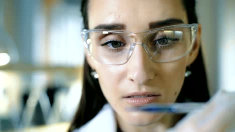 Young-female-scientist-holding-test-tube-with-liquid-sample-making-research-in-clinical-laboratory