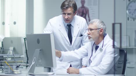 Senior-Doctor-and-His-Assistant-Discuss-Patient's-Log-on-Personal-Computer.-In-Slow-Motion.