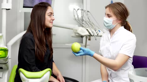 Dentista-mujer-joven-con-manzana-verde-al-paciente-sano-y-feliz-después-de-los-procedimientos